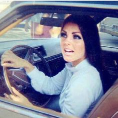 a woman sitting in the driver's seat of a car with her hand on the steering wheel