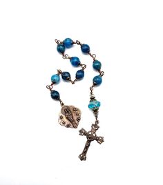 "Beautiful, handcrafted vintage-inspired Catholic Heirloom Tenner Rosary with large Pacific Blue Apatite gemstones. Pater bead is an Aquamarine Czech glass bead with Czech glass accent beads and Antique Brass bead caps. Each bead is wire wrapped using sturdy Vintage Bronze colored wire for strength and durability. The intricate design of the crucifix and medal are antique-styled bronze replicas giving the Rosary that \"Old World\" finish. Specifics:    *Ave Beads: Pacific Blue Apatite gemstones 10mm    *Pater Bead: Aquamarine Czech glass 14x9mm with Czech glass accent beads 2-4mm    *Caps and Spacers: Antique Brass    *Wire: 20-gauge Vintage Bronze colored enamel coated copper wire    *Crucifix: Solid Bronze Old Roma Ornate Crucifix (1 5/8 inches)    *Center: Solid Bronze Queen of Heaven 9 Handmade Bohemian Kyanite Jewelry, Handmade Rustic Blue Jewelry, Bohemian 8mm Beads Jewelry For Crafting, Bohemian 8mm Bead Jewelry For Crafting, Rustic Blue Jewelry With Natural Stones, Queen Of Heaven, Pacific Blue, Blue Apatite, Bead Caps