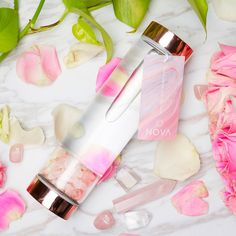 a pink and white bottle next to flowers on a marble surface with petals around it