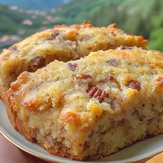 a close up of a person holding a piece of cake on a plate with mountains in the background