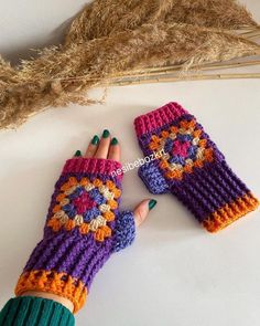 two crocheted mittens sitting on top of a table next to a dried plant