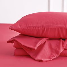 two red pillows stacked on top of each other with pink sheets and pillowcases