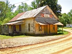 an old run down building sitting on the side of a dirt road in front of trees