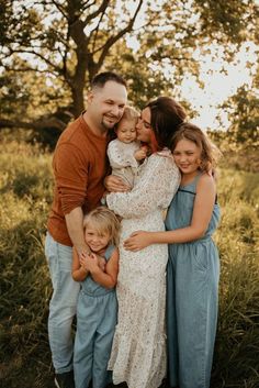 a man and two women are hugging their children in the grass with trees behind them