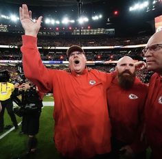 two men in red shirts are standing on the sidelines at a football game with their hands up