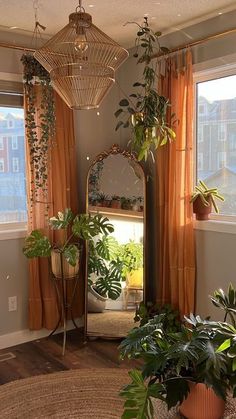 a living room filled with lots of plants next to a window covered in orange drapes