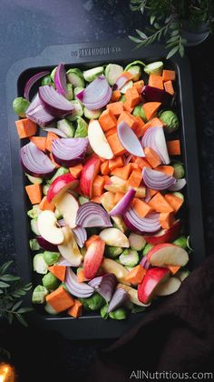 chopped vegetables are arranged in a square tray on a dark surface next to a lit candle