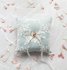 a ring pillow on a white surface with pink flowers around it and petals scattered all over the floor