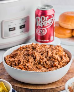 a white bowl filled with shredded meat next to a can of dr pepper's