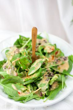 a white plate topped with green salad and a wooden spoon on top of the bowl