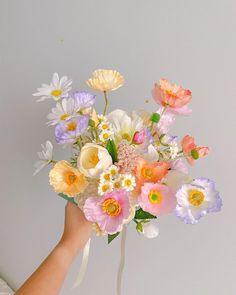 a hand holding a bouquet of flowers with white and pink blooms in the center, on a gray background