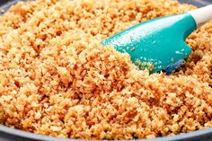 a blue spatula scooping some food out of a pan filled with brown crumbs