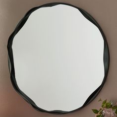 a round mirror mounted to the side of a wall next to a potted plant