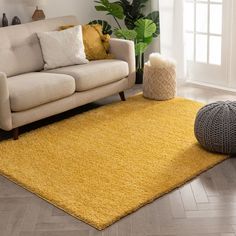 a living room with a white couch and yellow rug on the floor in front of a window