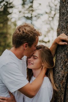 a man and woman hugging against a tree