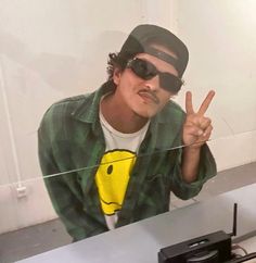 a man with sunglasses making the peace sign while sitting in front of a computer desk