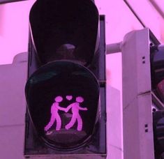 a traffic light with a pink sticker on it's face and two people holding hands