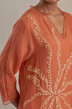 a woman wearing an orange top with beading on it