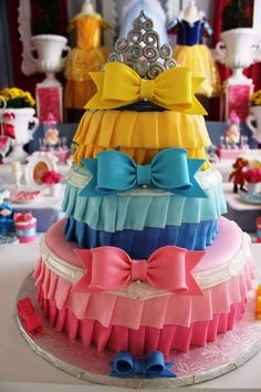 a multi - colored cake with bows and a tiara on top is sitting on a table