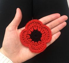 a hand holding a crocheted red and black flower