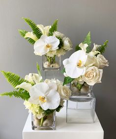 three clear vases with white flowers and greenery