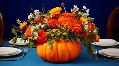 an arrangement of flowers and greenery in a pumpkin shaped centerpiece on a blue table cloth