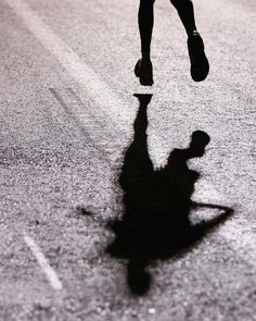 a person is running down the street with their shadow on the ground and one foot in the air