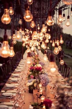 a long table with lots of lights hanging from it's ceiling and flowers in the center