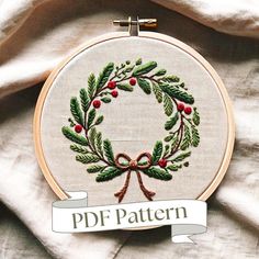 an embroidered christmas wreath with holly and red berries is displayed in front of a white blanket