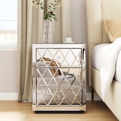 a bed with a white headboard next to a window and a silver mirrored cabinet