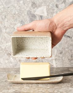 a hand holding a block of cheese over a plate with chopsticks on it