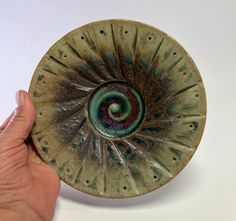 a hand is holding a green and brown bowl with a spiral design on the bottom