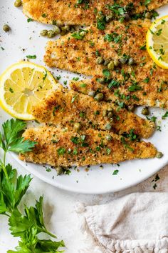 fish fillets on a white plate with lemons and parsley garnish