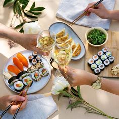 several people are eating sushi and drinking wine at a table with chopsticks