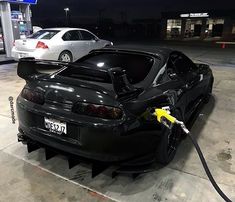 a black car is hooked up to an electric charger in a parking lot at night