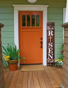 an orange front door with the words home on it and potted plants in front