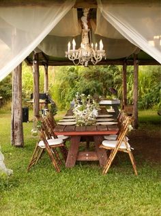 a wooden table with chairs under a white cloth covered structure in the middle of grass