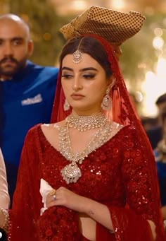 a woman in red dress and headpiece standing next to other people