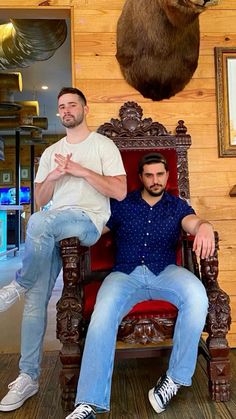 two men are sitting on a chair in front of a fake animal