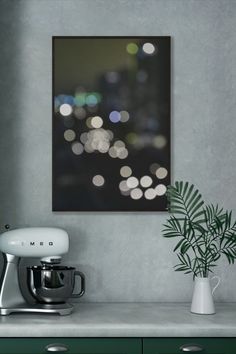 a kitchen counter with a mixer, potted plant and painting hanging on the wall