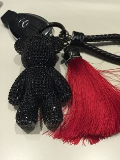 a black and red teddy bear keychain on a white surface with a red tassel