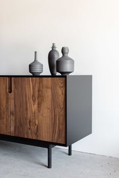 two vases sitting on top of a wooden cabinet in front of a white wall