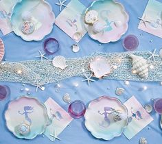 a table topped with plates and seashells on top of a blue cloth covered table