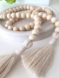 a wooden beaded necklace with tassels on a white table next to a plant