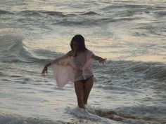 a woman walking into the ocean with her arms spread out in front of her body