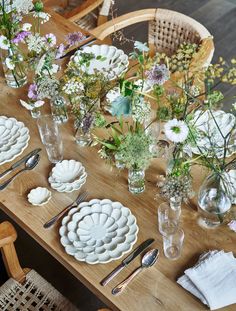 a wooden table topped with plates and vases filled with flowers