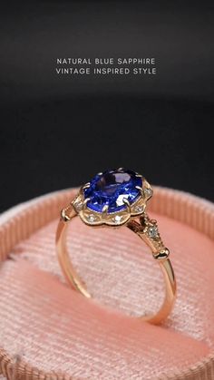 a ring with a blue sapphire in it sitting on a pink velvet cushioned box