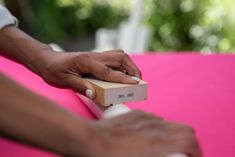 a person is using a small device on a pink surface