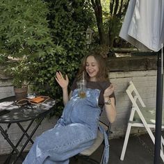 a woman in overalls sitting on a patio chair