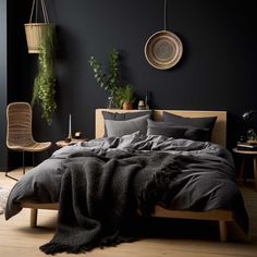 a bedroom with black walls and wooden flooring is pictured in this image, there are plants hanging on the wall above the bed